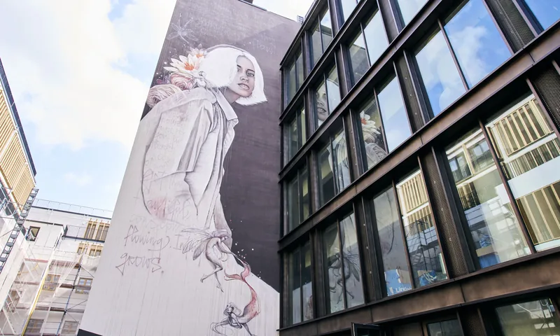 Glasfassade des KALLE Neukölln mit großem Wandbild, Blick von unten