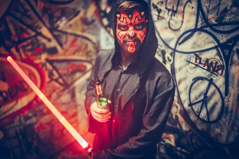 Maskierter Gast mit rotem Lichtschwert vor Graffiti-Wand