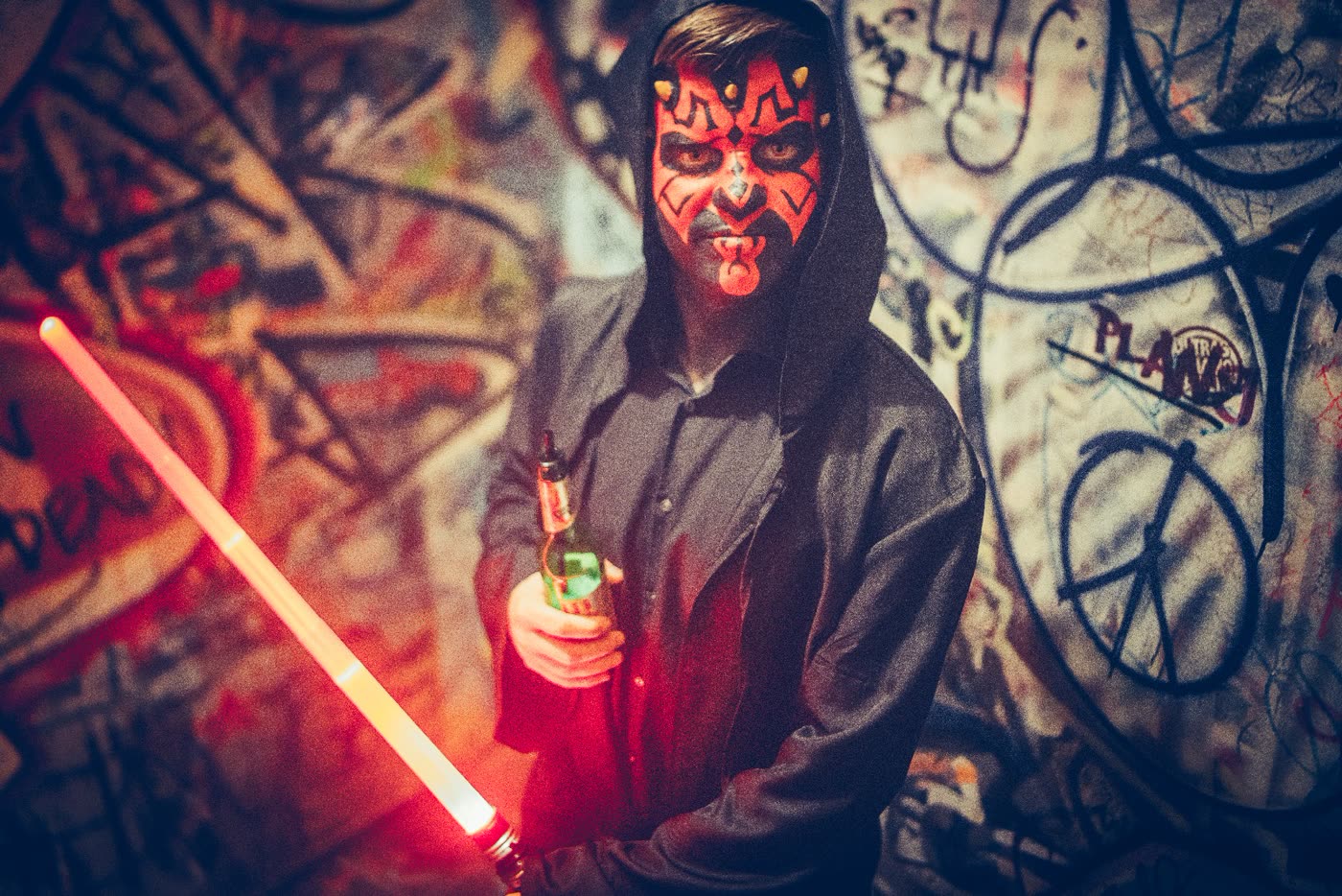 Maskierter Gast mit Lichtschwert vor Graffiti-Wand
